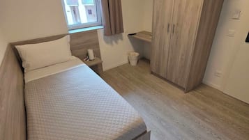 Un dormitorio con cama, armario, ventana y una mesita.