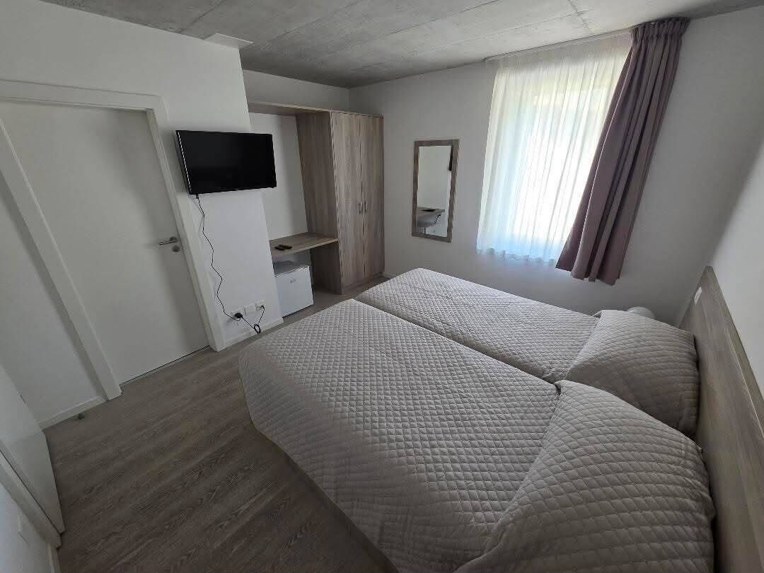 A bedroom with two beds, a TV, a wardrobe, and a window with curtains.