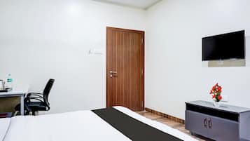 A hotel room with a bed, a desk, a chair, a TV mounted on the wall, and a cabinet with a vase of flowers.