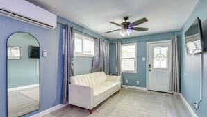 Una habitación con un sofá blanco, un ventilador de techo, un espejo grande y una puerta con ventana.