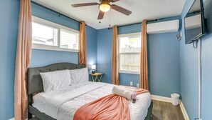 Un dormitorio con cama, ventilador de techo, aire acondicionado, televisor y ventana con cortinas.