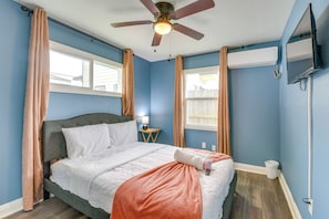 Ein Schlafzimmer mit Bett, Deckenventilator, Klimaanlage, Fernseher und einem Fenster mit Vorhängen.
