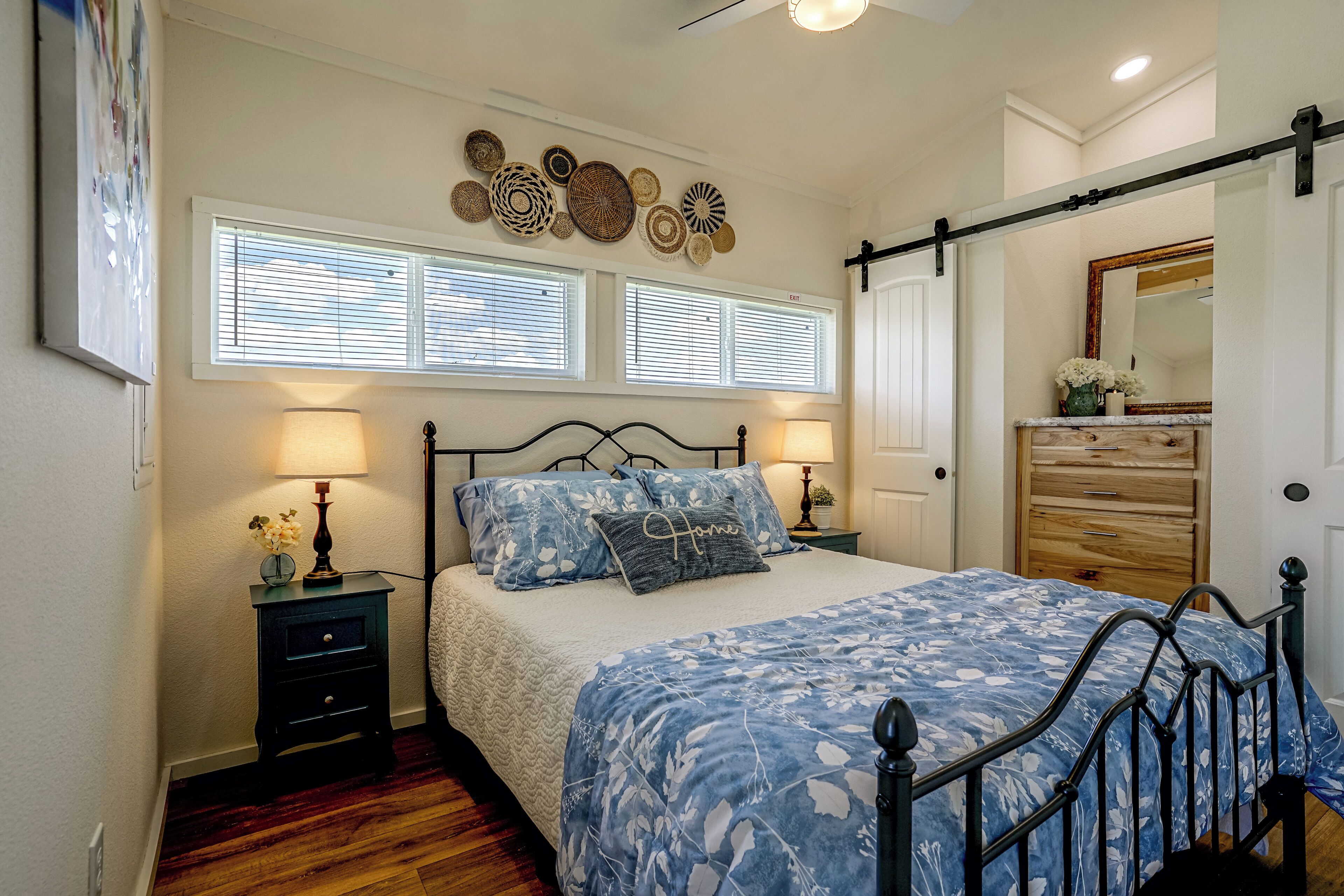 A bedroom with a bed, two bedside tables, a dresser, a mirror, and wall decorations.