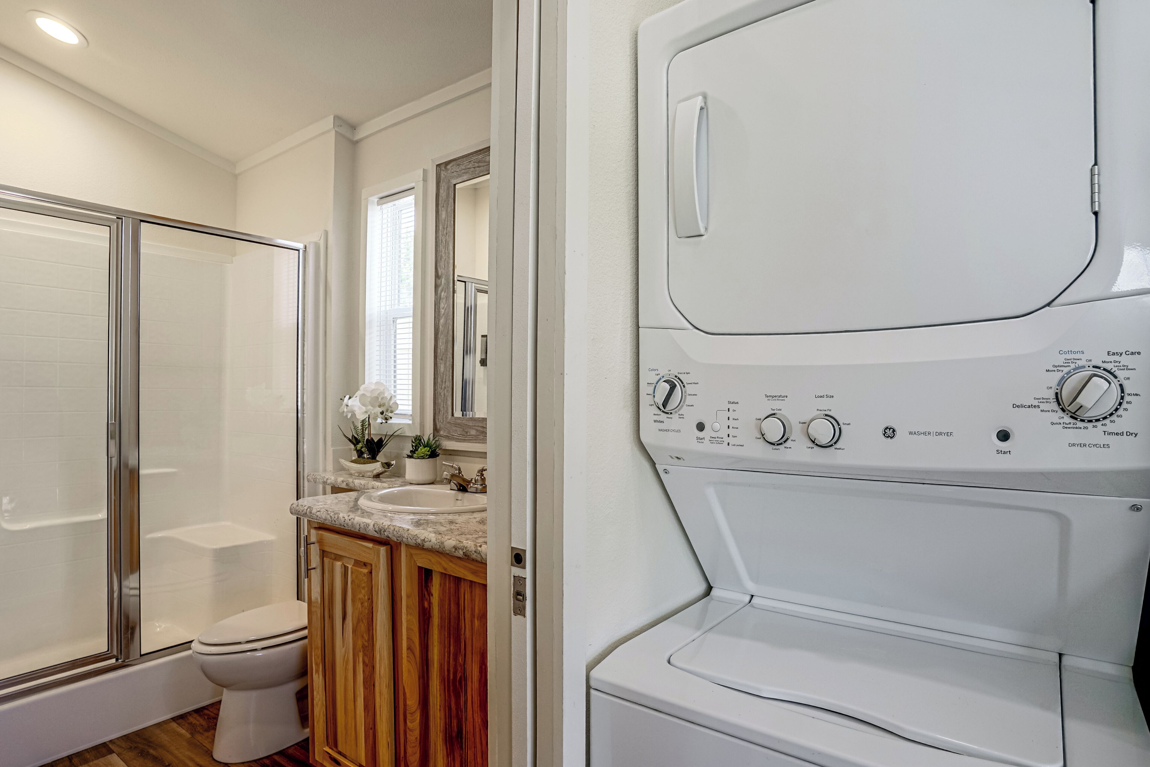 A modern bathroom with a walk-in shower, a toilet, and a built-in washer/dryer unit.