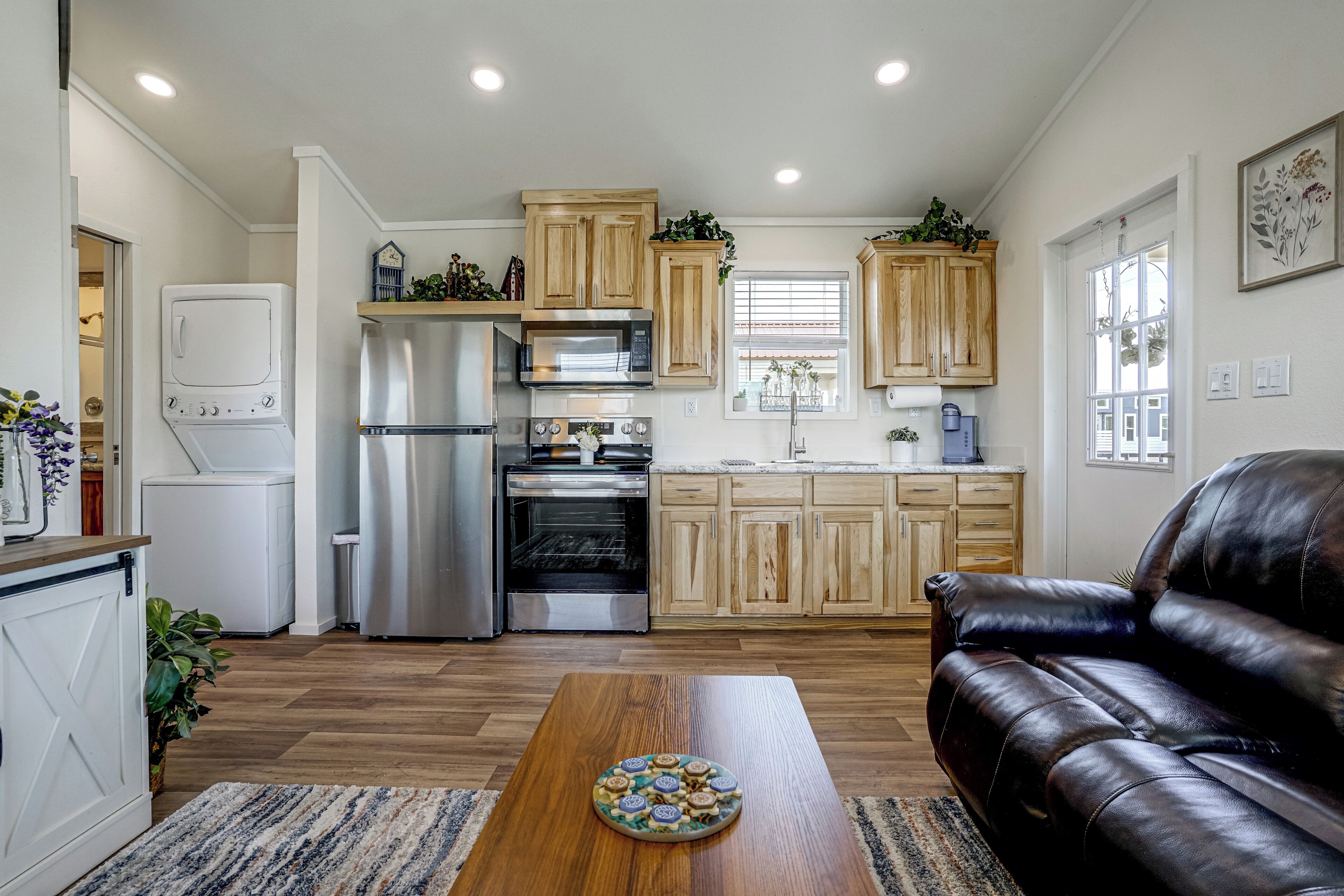 A modern kitchen with stainless steel appliances, wooden cabinets, and a black leather sofa in the living area.
