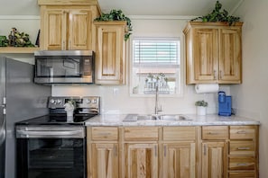 A kitchen with wooden cabinets, stainless steel appliances, a window with blinds, and a blue water dispenser.