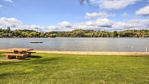 En picknickplats vid sjön med ett träbord och bänkar, omgiven av en gräsyta och med utsikt över en sjö där svanar simmar.