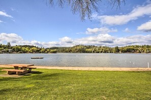 Ein Picknickplatz am Seeufer mit Holztisch und Bänken, umgeben von einer Wiese und Blick auf einen See mit Schwänen.