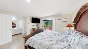 Ein Schlafzimmer mit einem Bett, einem Fernseher, einer Tür zu einem Balkon und einem Nachttisch mit einer Lampe.