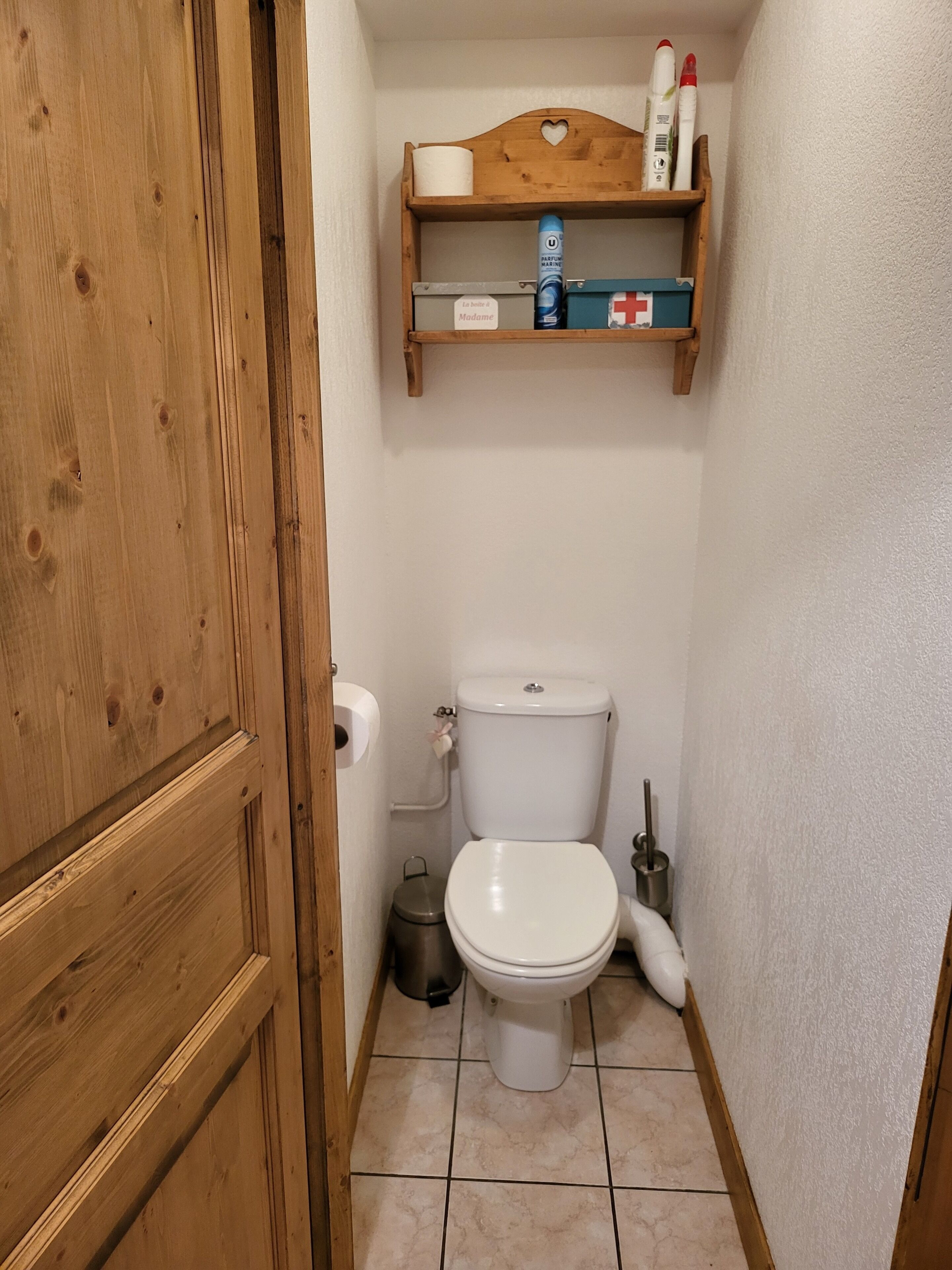 Pieni kylpyhuone, jossa on puuovi, wc-istuin, hylly, jossa on hygieniatuotteita, ja roskakori.