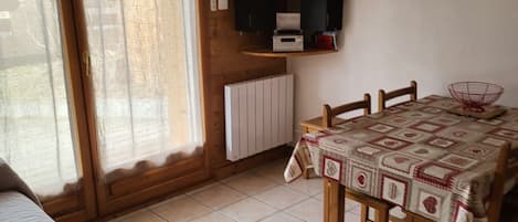 A room with a bed, a dining table with chairs, a television mounted on the wall, and a radiator.