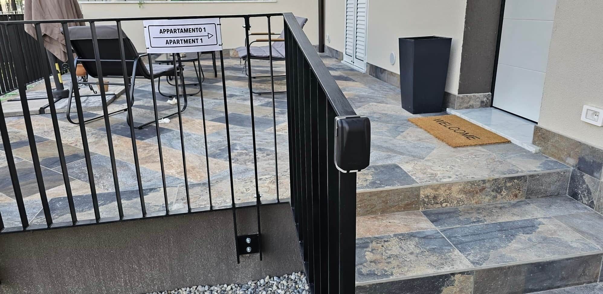 Une entrée fermée par un portail donnant accès à un immeuble d’appartements, avec une pancarte indiquant « APPARTEMENT 1 ».