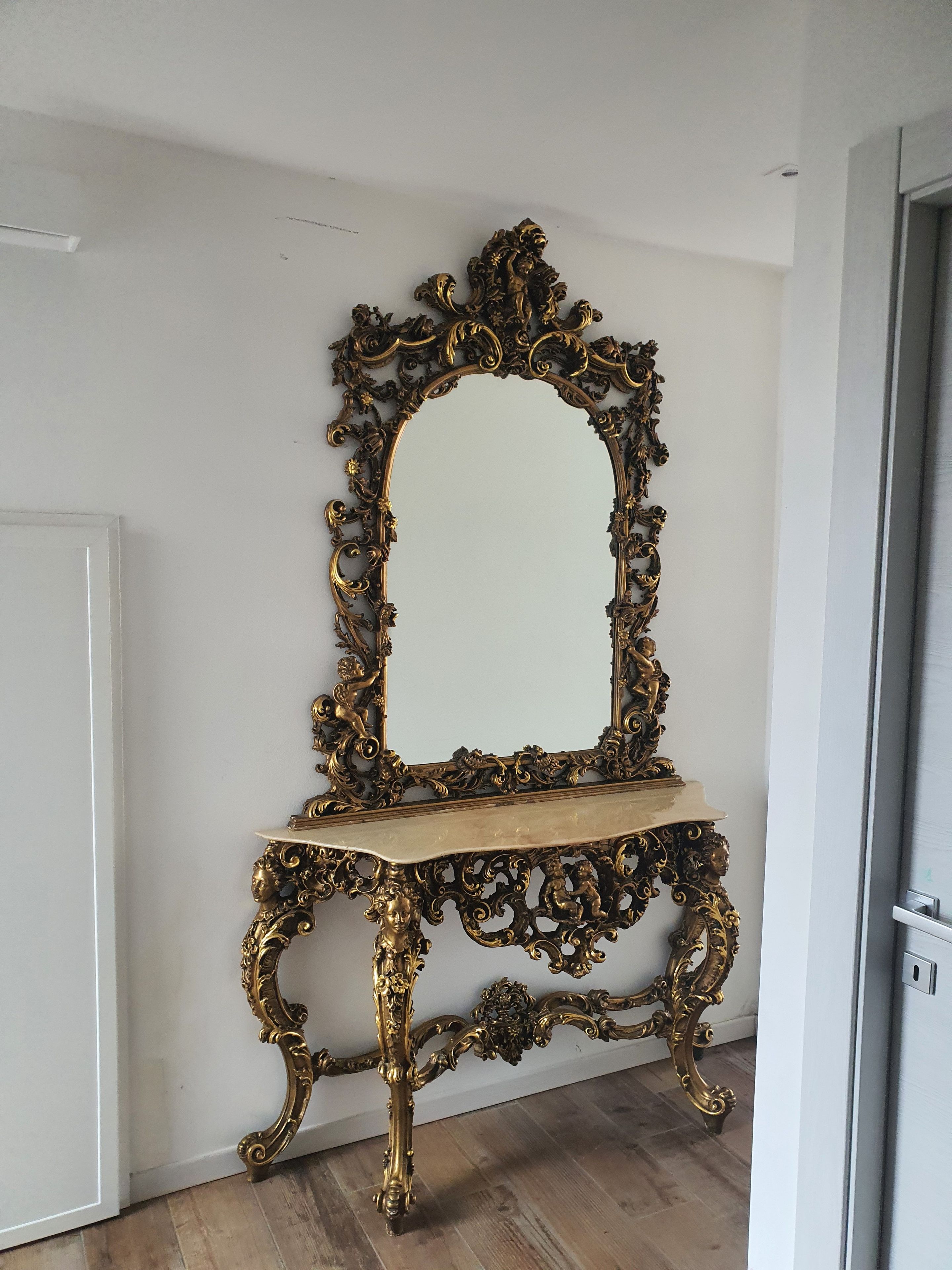 A mirror with an ornate gold frame and a wooden stand, mounted on a white wall.