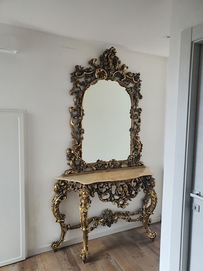 A mirror with an ornate gold frame and a wooden stand, mounted on a white wall.