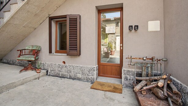 A building entrance with a wooden door, a window with shutters, a chair, and a pile of logs.