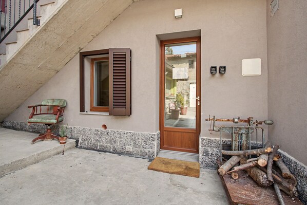 A building entrance with a wooden door, a window with shutters, a chair, and a pile of logs.