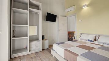 A bedroom with a bed, a wardrobe, a television, and a painting on the wall.