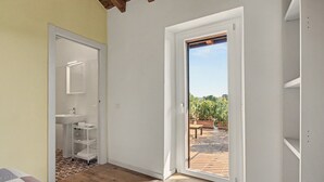 A room with a bathroom, a wooden floor, and a door leading to an outdoor area with plants.