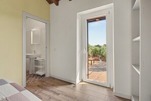 A room with a bathroom, a wooden floor, and a door leading to an outdoor area with plants.