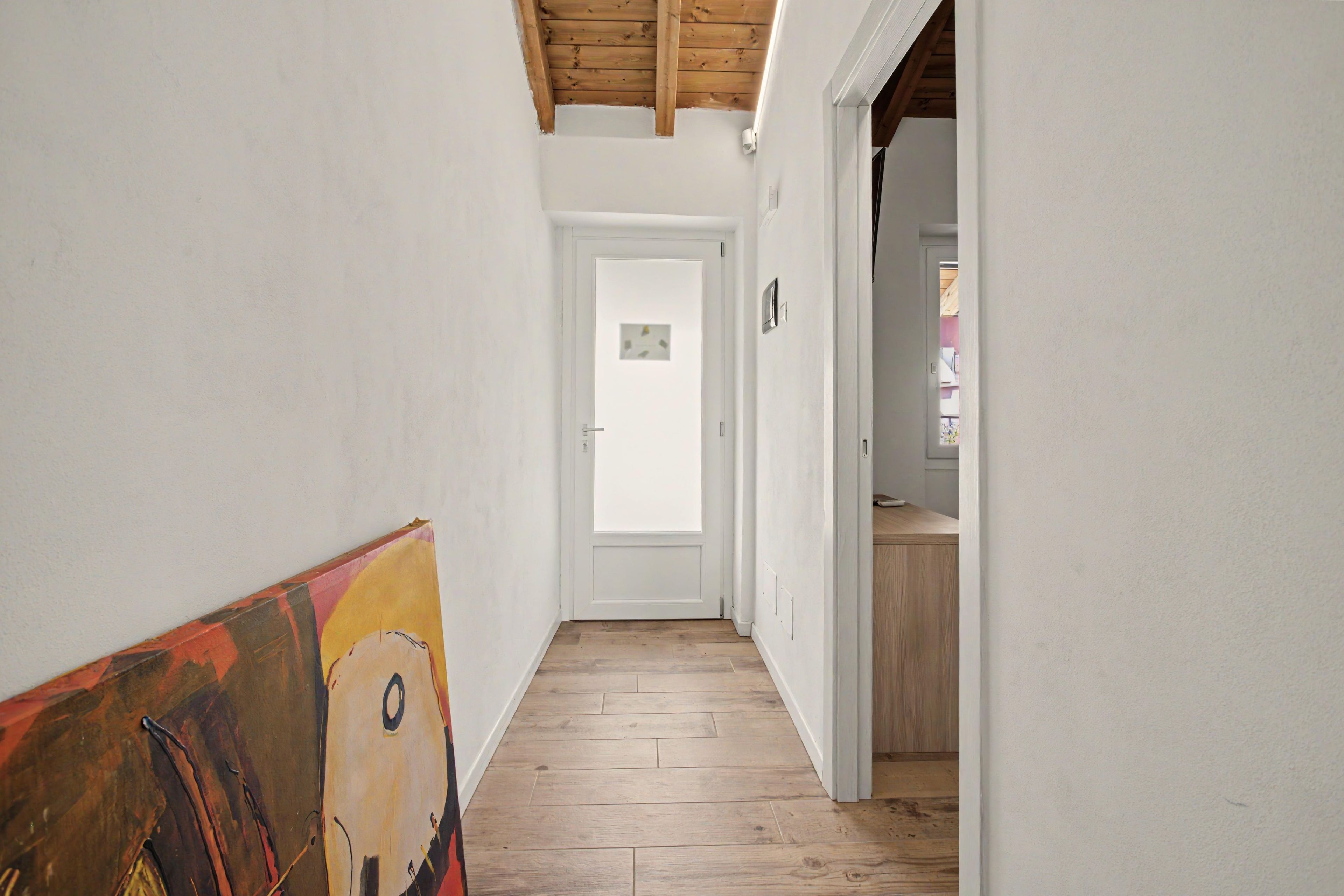 A narrow hallway with wooden flooring and white walls, leading to a door with a small window.