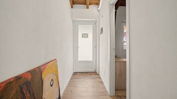 A narrow hallway with wooden flooring and white walls, leading to a door with a small window.