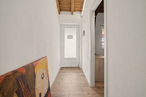 A narrow hallway with wooden flooring and white walls, leading to a door with a small window. - Double Room in 'La Cà De' Mi Vecc' with Open Terrace (Costa)