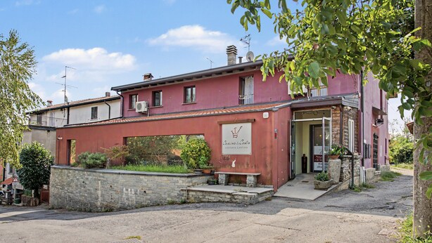 Un edificio con fachada roja, un muro de piedra en primer plano y un letrero que indica un restaurante.