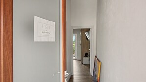 Un pasillo con una puerta a la izquierda, un cartel enmarcado en la pared y una zona de cocina al fondo.
