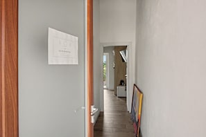 A hallway with a door on the left, a framed sign on the wall, and a kitchen area in the distance.