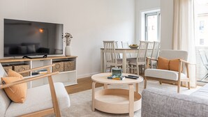 En moderne stue med et fladskærms-tv, et spisebord med stole, et rundt sofabord og en sofa.