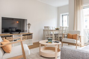 Ein modernes Wohnzimmer mit Flachbildfernseher, einem Esstisch mit Stühlen, einem runden Couchtisch und einer Couch.