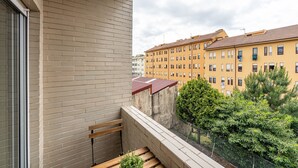 En balkon med træbænk, metalgelænder og udsigt til en gul bygning med mange vinduer.