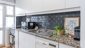 Et moderne køkken med hvide skabe, en backsplash i sort flise, en stålvask og en Siemens opvaskemaskine.