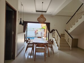 A dining area with a table and chairs, a staircase, and a view of the outdoors. - Saren Kayutulang, Quiet 3BR Pool Villa (Badung)