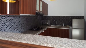 Cozinha com armários de madeira, bancada de granito, geladeira de aço inoxidável e iluminação pendente.