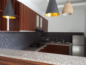 A kitchen with wooden cabinets, a granite countertop, a stainless steel refrigerator, and pendant lighting. - Saren Kayutulang, Quiet 3BR Pool Villa (Badung)
