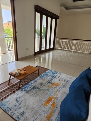 A spacious room with a large sliding glass door leading to a balcony, a wooden coffee table with books, and a patterned rug. - Saren Kayutulang, Quiet 3BR Pool Villa (Badung)