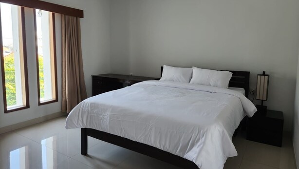 Quarto com cama, mesas de cabeceira, abajur e janela com cortinas.