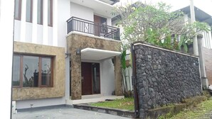 Uma casa moderna de dois andares com fachada de pedra, uma varanda e um pequeno jardim frontal.