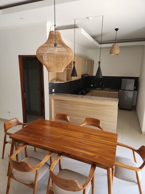 A modern kitchen with a central island, wooden dining table, and chairs. - Saren Kayutulang, Quiet 3BR Pool Villa (Badung)