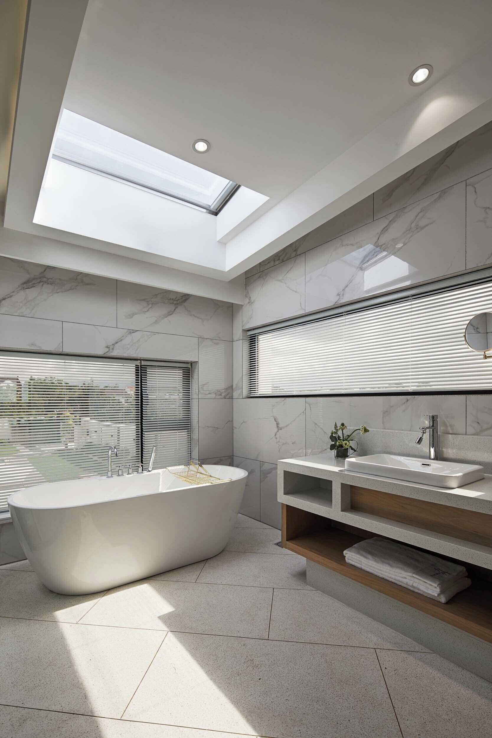A modern bathroom with a freestanding bathtub, a vanity with a mirror, and a skylight above.