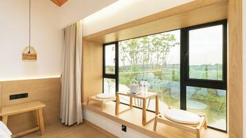 A modern room with a large window, a wooden bench, a small table with a kettle and bottles, and a hanging light fixture.