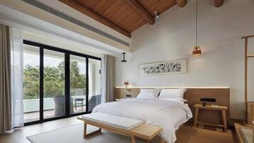 A modern bedroom with a large bed, a bench, a bedside table, and a view of the outdoors.