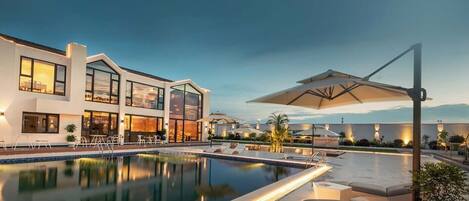 A modern pool area with a clear view of the pool, lounge chairs, and a building with large windows.