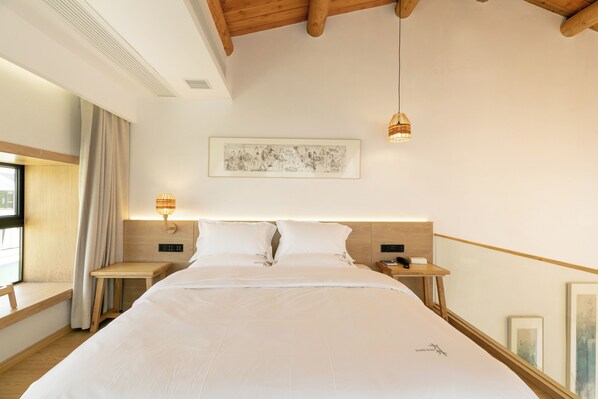 Une chambre d’hôtel avec un grand lit, des tables de chevet, une fenêtre avec des rideaux, une œuvre d’art accrochée au mur et un ventilateur de plafond.