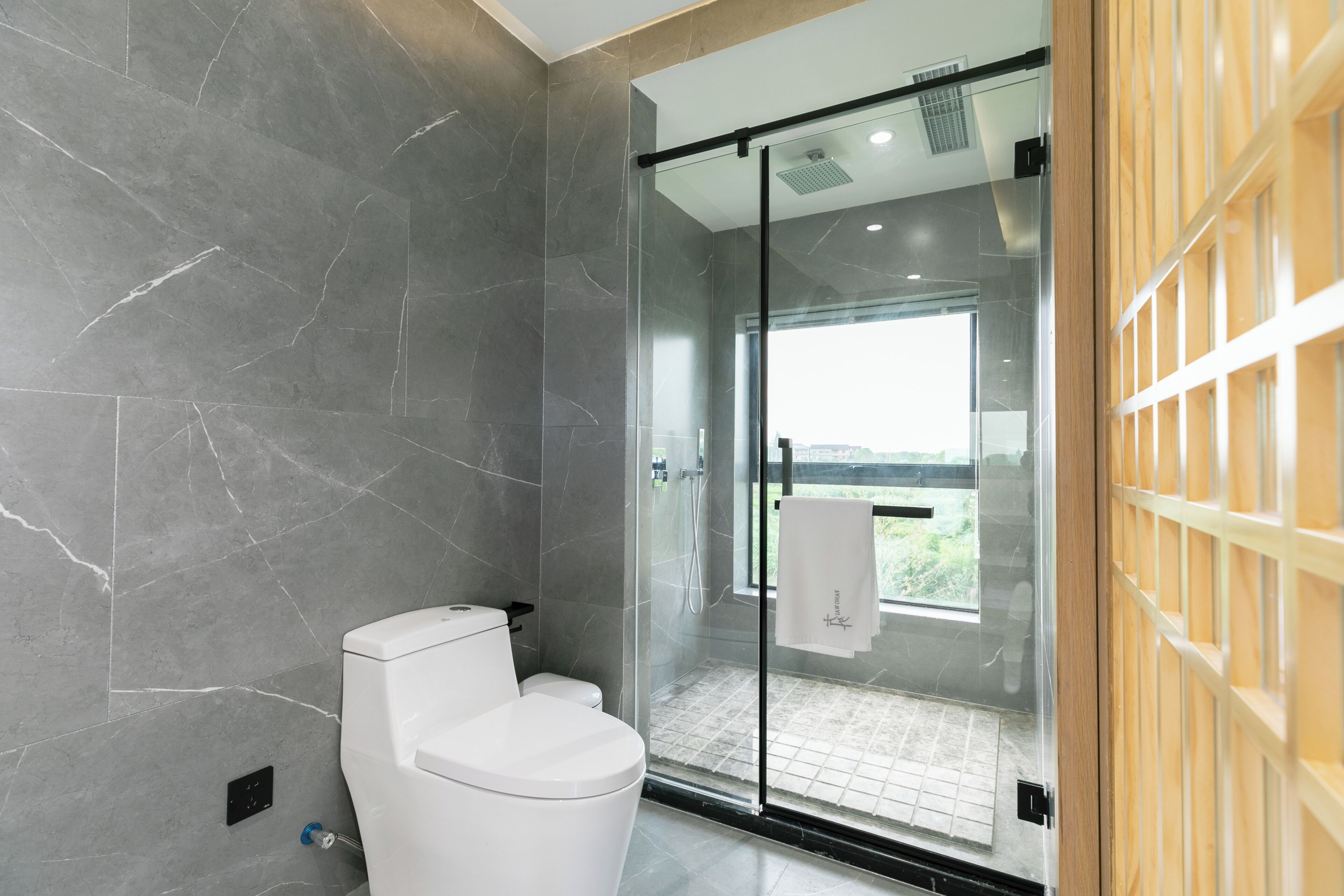 A modern bathroom with a glass shower enclosure, a white toilet, and a view of the outdoors.