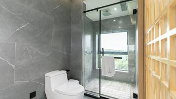 A modern bathroom with a glass shower enclosure, a white toilet, and a view of the outdoors.