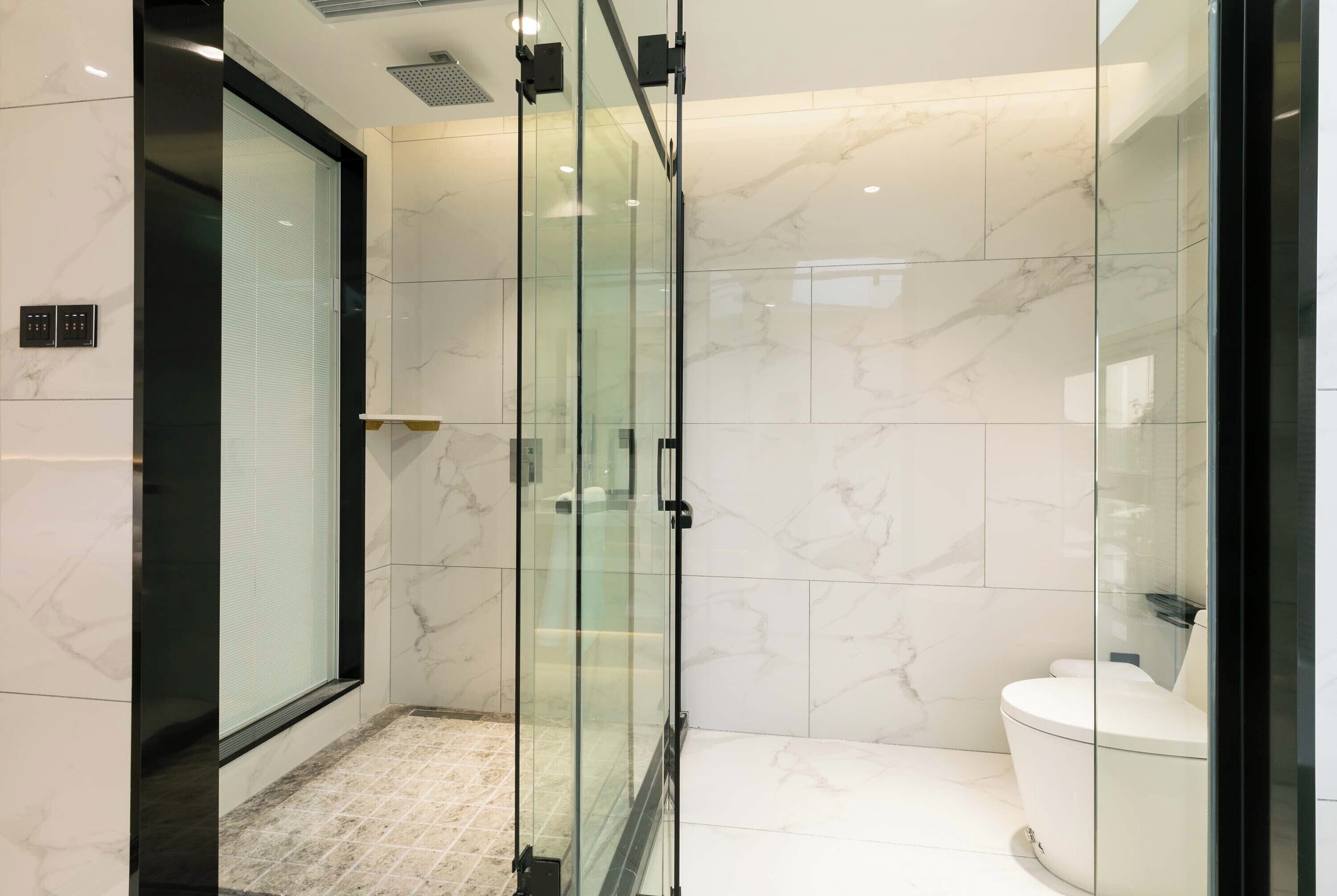 Ein modernes Badezimmer mit Duschkabine aus Glas, Toilette und Marmorboden.