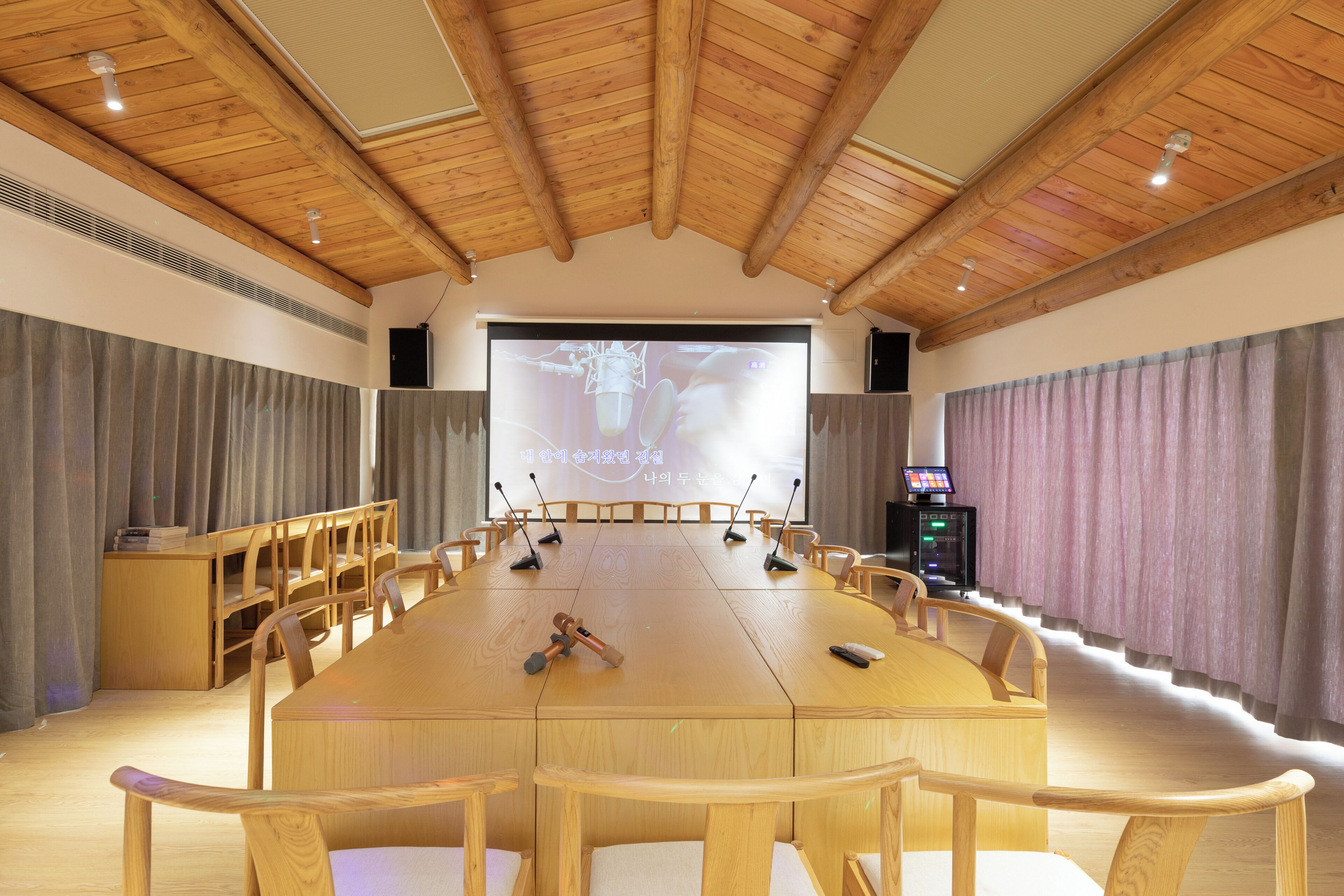 Een vergaderruimte met een grote houten tafel, stoelen, een projectiescherm en een geluidsinstallatie.