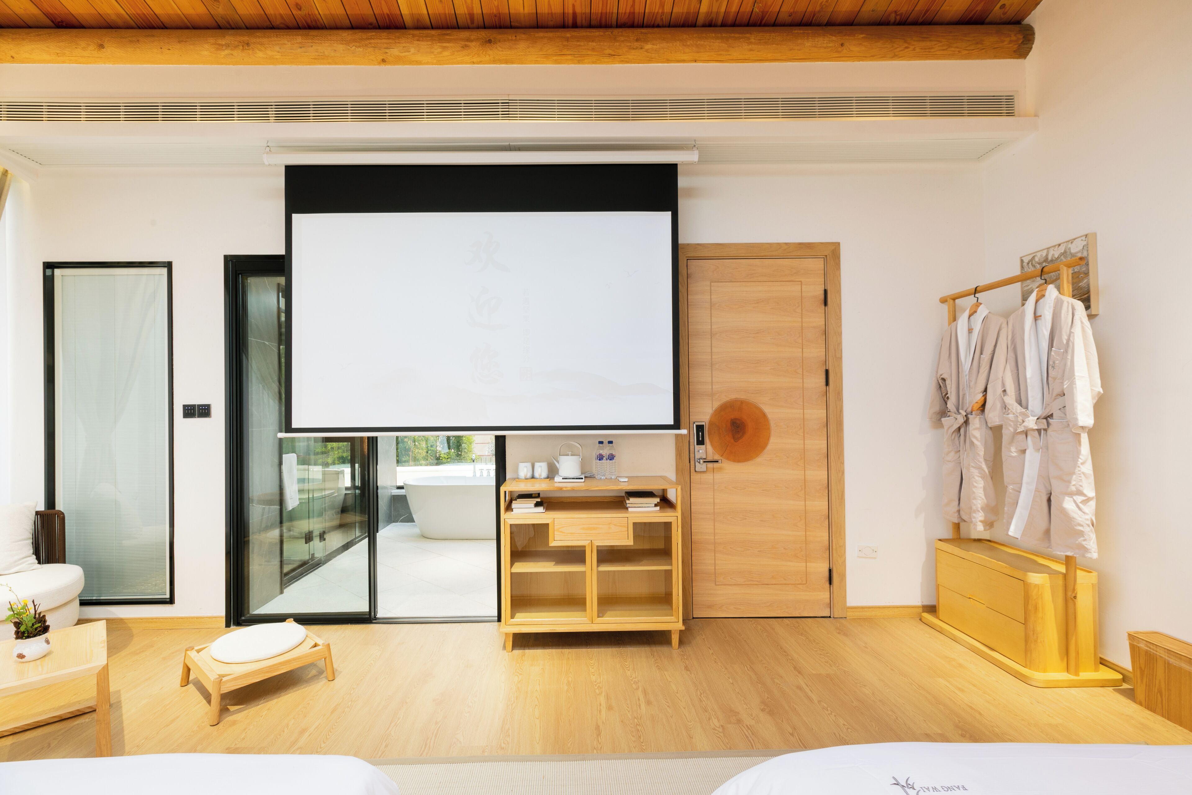 A modern room with a large bed, a wooden desk, a bathtub, and a wardrobe with robes.